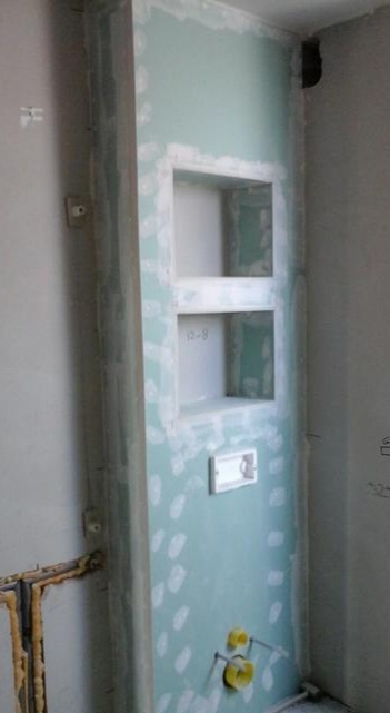 Ściana z płyty kartonowo-gipsowej z wnękami, wstępnie zagruntowana, widoczne instalacje hydrauliczne w dolnej części ściany.