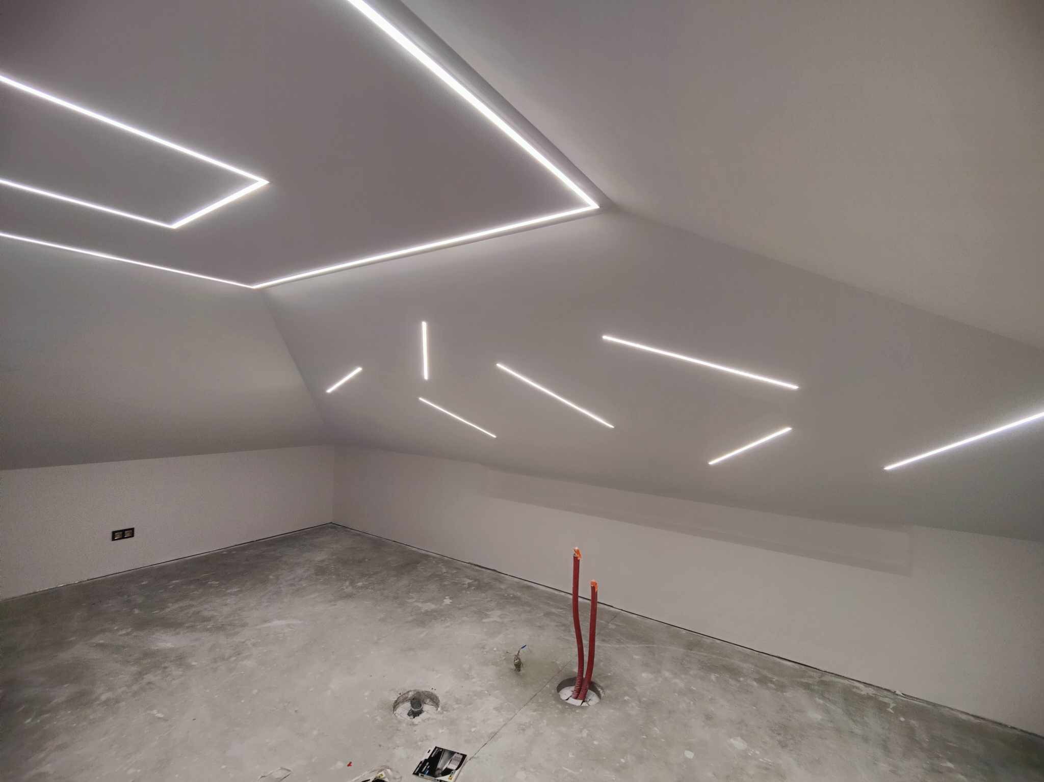 Poddasze w trakcie wykańczania z nowoczesnym oświetleniem LED na suficie, widoczne przewody instalacji elektrycznej wystające z podłogi.