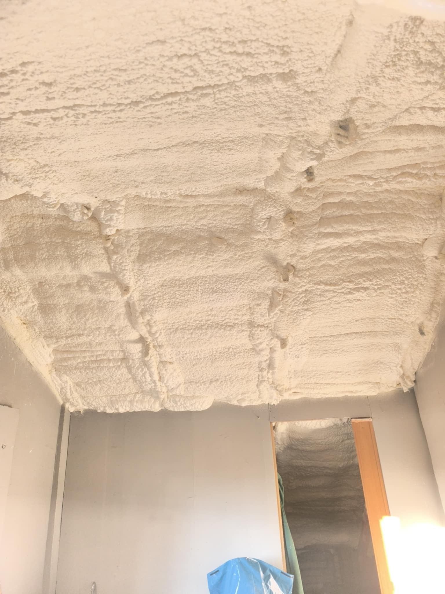 Ocieplenie pianką PUR na suficie i ścianach wewnątrz pomieszczenia, widoczne nierówności i struktura piany, jasne oświetlenie.