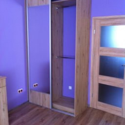 MR Meble Magdalena Okońska - Jasna szafa wnękowa z przesuwnymi lustrzanymi drzwiami w pokoju o fioletowych ścianach i drewnianej podłodze, widoczny fragment drzwi z szybami.