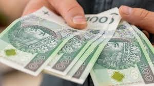 Dłoń trzymająca plik banknotów 100 zł z wizerunkiem króla Władysława Jagiełły, widoczne delikatne załamania papieru i charakterystyczny zielony element zabezpieczający.