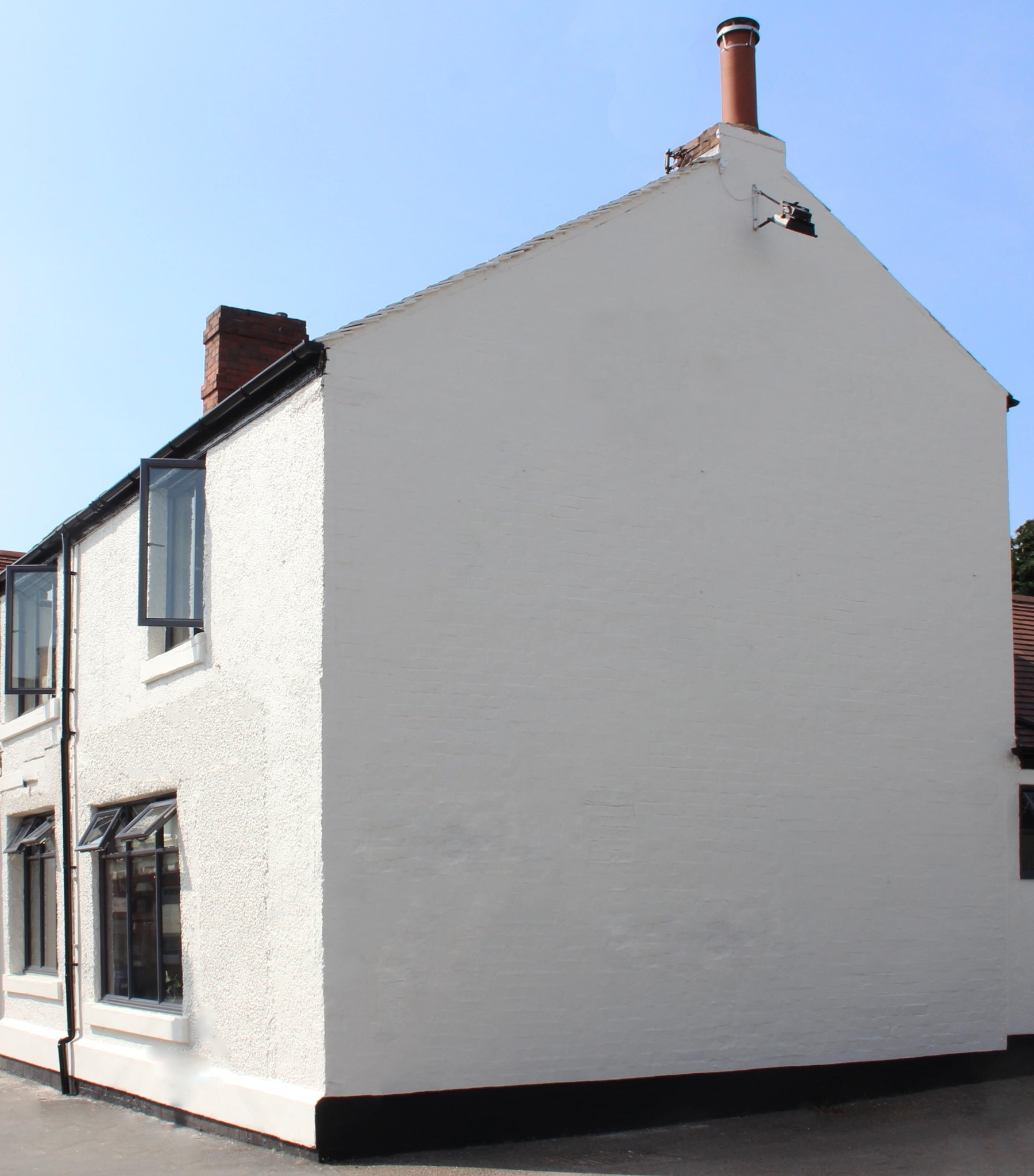 Odnowiona elewacja dwukondygnacyjnego domu z ceglanymi kominami, pomalowana na biało, z czarną lamperią i oknami z czarną ramą.