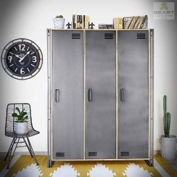 P.h.u.p.seart - Metalowa szafa trzydrzwiowa w stylu industrialnym z drewnianymi akcentami, ustawiona na żółto-białym dywanie w geometryczne wzory, obok czarne krzesło z rośliną i duży zegar na ścianie.