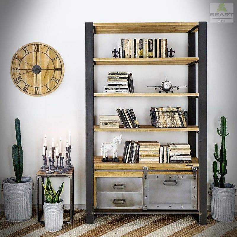 Regał z metalową ramą i drewnianymi półkami, uzupełniony o metalowe szuflady z przesuwnymi drzwiczkami, na tle ściany z zegarem i kaktusami w metalowych donicach.