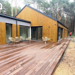 Gwdt Sp. z o.o. - Nowoczesny dom z drewnianą elewacją i tarasem, otoczony lasem. Widoczne krzesła na tarasie i częściowo zrealizowana zabudowa tarasu z boku budynku.