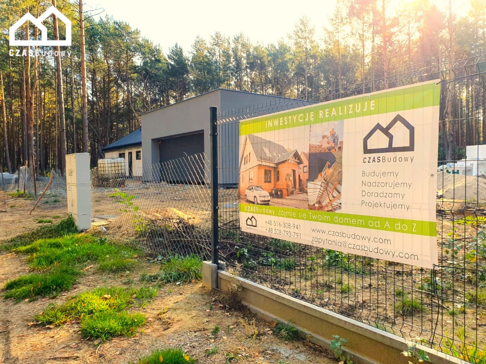 Baner firmy budowlanej 'CzasBudowy' na tle budowanego domu w lesie. Na banerze wizualizacje domów i hasło 'Inwestycje Realizuje'.