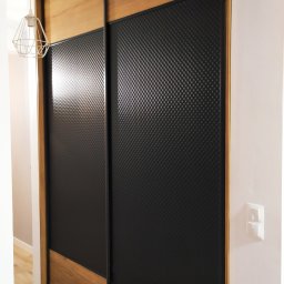 Molenda Meble Na Wymiar - Nowoczesna szafa przesuwna z drewnianymi elementami i czarnymi panelami z fakturą, oświetlona wiszącą lampą drucianą.