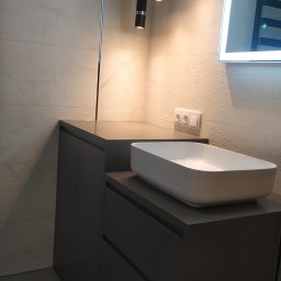Molenda Meble Na Wymiar - Nowoczesna łazienka z szarą szafką pod umywalkę nablatową, oświetlona wiszącymi lampami tubami i lustrem z podświetleniem LED.