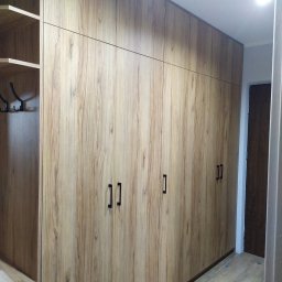 Molenda Meble Na Wymiar - Wysoka zabudowa szafy z frontami imitującymi drewno, z czarnymi, prostokątnymi uchwytami, po lewej stronie otwarta garderoba z wieszakami.