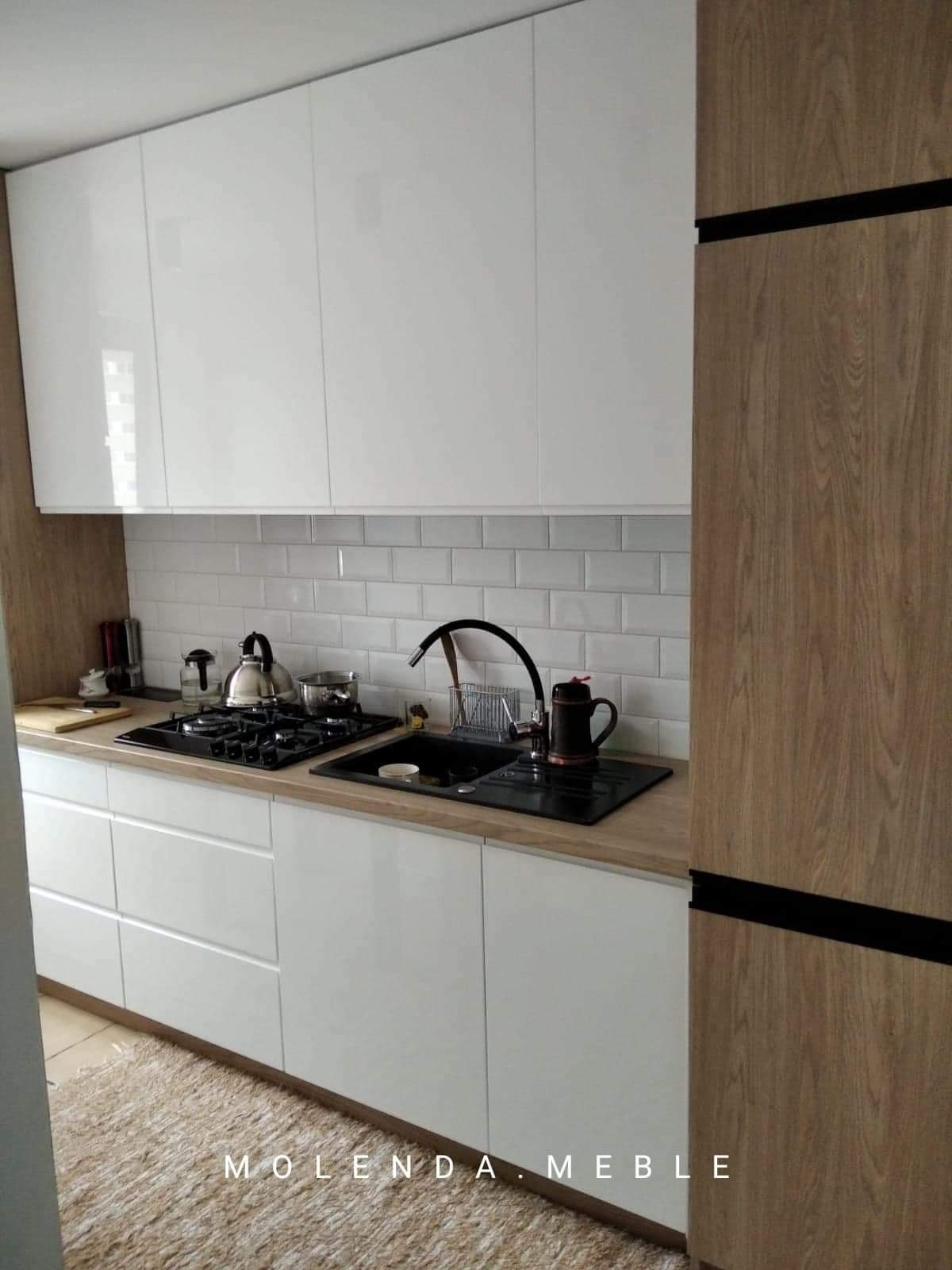 Nowoczesna kuchnia z białymi, lakierowanymi frontami szafek, drewnianym blatem i czarną armaturą, widok na płytę grzewczą i zlew, na blacie czajnik i akcesoria kuchenne.
