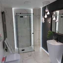 Apis Sp. z O.O. Grupa Sbs - Nowoczesna łazienka z kabiną prysznicową typu walk-in z czarnymi profilami, wiszącą toaletą z podestem, umywalką wolnostojącą i marmurowymi płytkami.
