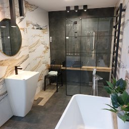 Apis Sp. z O.O. Grupa Sbs - Nowoczesna aranżacja łazienki z wolnostojącą wanną, wysoką umywalką na postumencie, kabiną prysznicową z czarnymi ramami i marmurowymi płytkami w odcieniach bieli i złota.