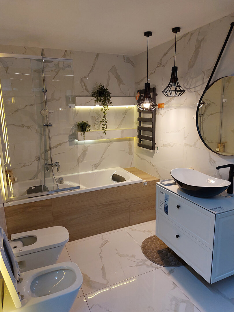 Nowoczesna aranżacja łazienki z wanną obudowaną drewnem, umywalką nablatową w kolorze czarno-białym, białą szafką z szufladami, wiszącą drabinką na ręczniki i dwoma lampami wiszącymi o ażurowych...