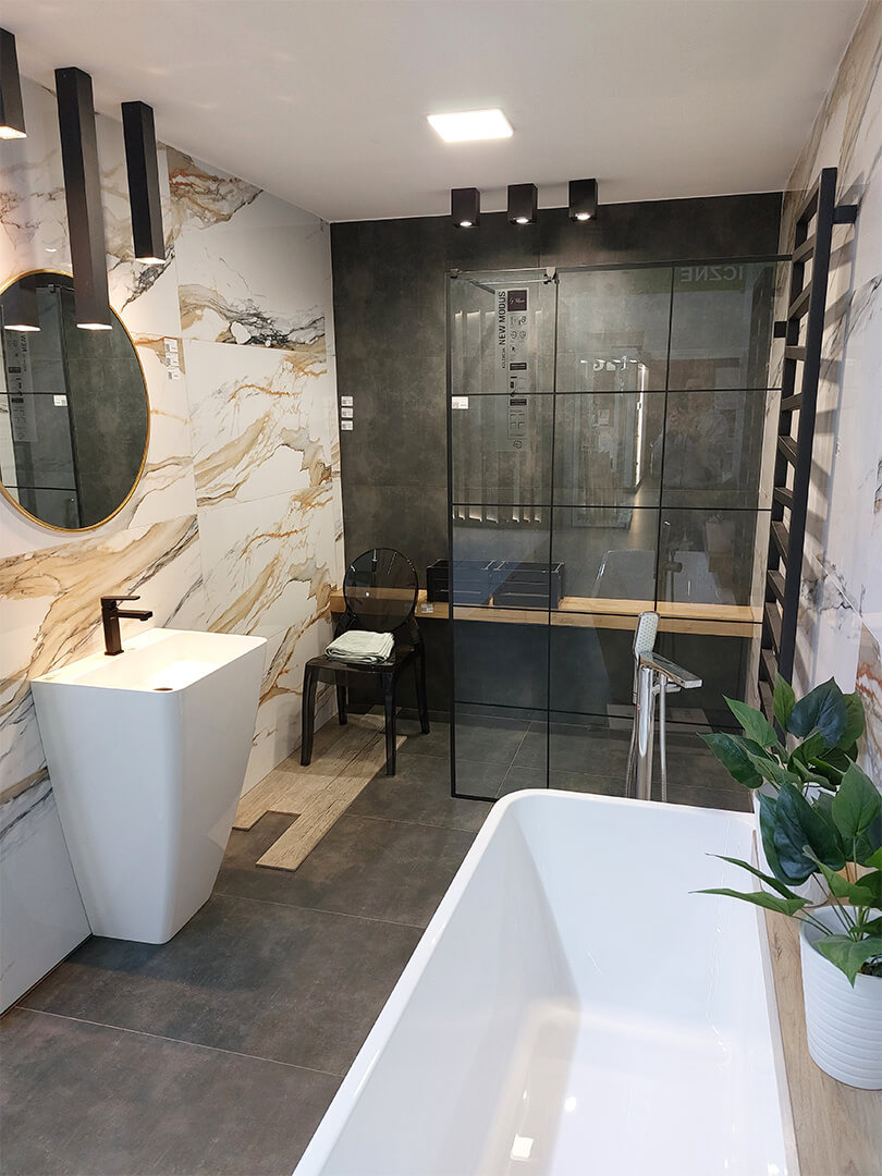 Nowoczesna aranżacja łazienki z wolnostojącą wanną, wysoką umywalką na postumencie, kabiną prysznicową z czarnymi ramami i marmurowymi płytkami w odcieniach bieli i złota.