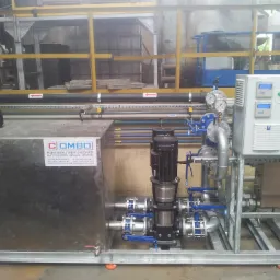 Kompleksowa instalacja chłodnicza przemysłowa z pompą Grundfos, zbiornikiem ze stali nierdzewnej i panelem sterowania Alref, widoczna na tle hali produkcyjnej z żółtymi barierkami.