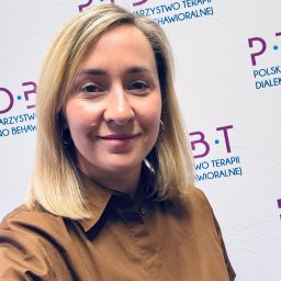 Promed Psychoterapia - Portret uśmiechniętej blondynki w brązowej koszuli na tle logo P.T.D.B.T. (Polskie Towarzystwo Terapii Dialektyczno-Behawioralnej).