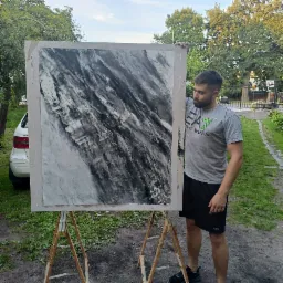 Mężczyzna prezentuje próbkę ściany z efektem dekoracyjnym imitującym marmur w odcieniach szarości, umieszczoną na drewnianym stojaku malarskim na zewnątrz.