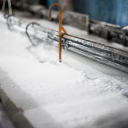 Metalowa konstrukcja zanurzona w białej, pieniącej się cieczy, prawdopodobnie proces czyszczenia lub obróbki powierzchniowej.