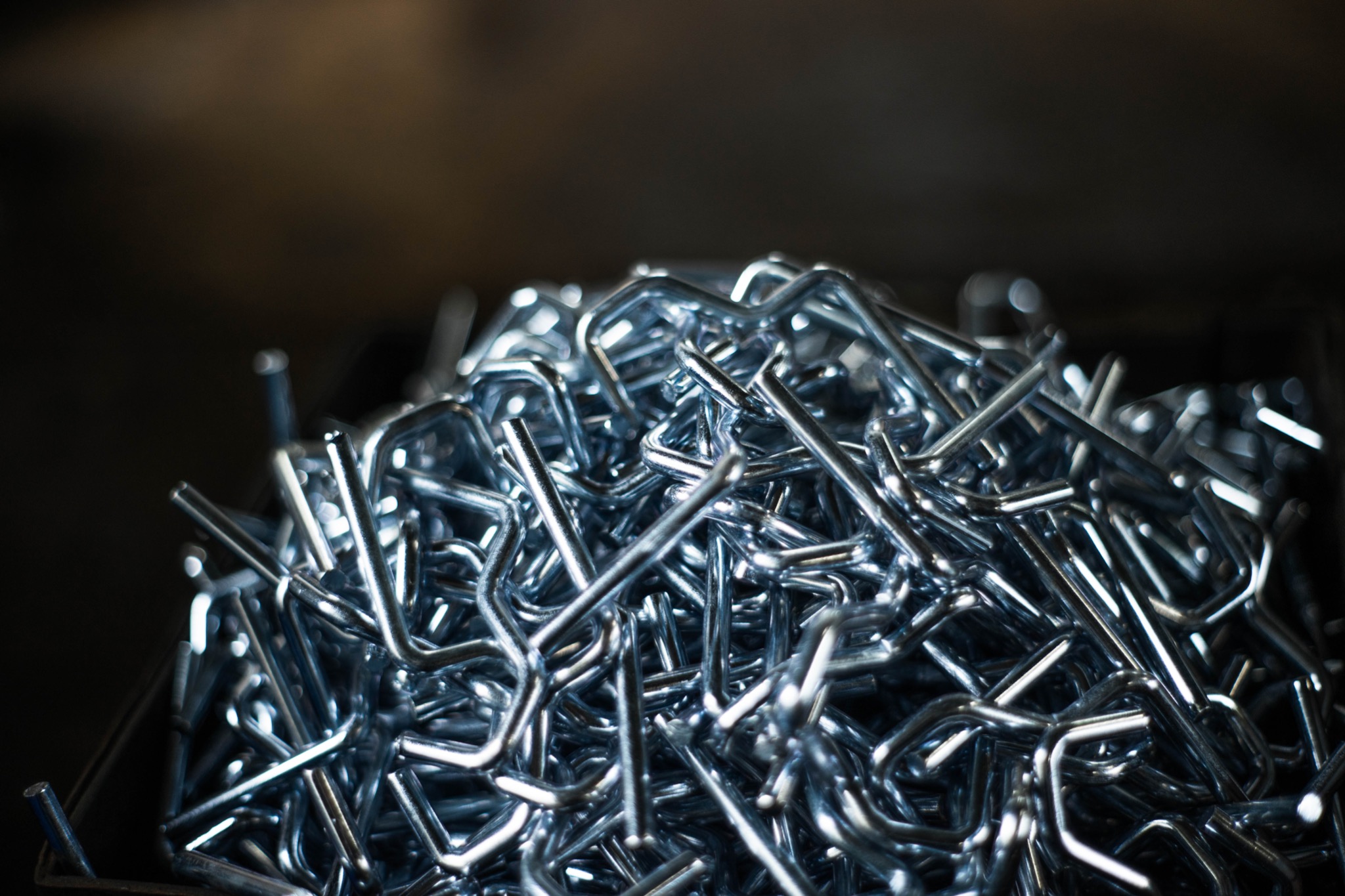 Stalowe, ocynkowane łączniki do siatki ogrodzeniowej, ułożone w stosie, widoczne z bliska w chłodnym oświetleniu.