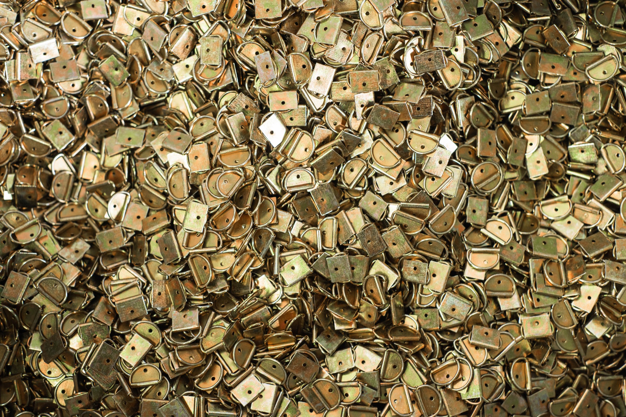 Gęsto ułożone, metalowe uchwyty spawalnicze w odcieniach złota i zieleni, z widocznymi otworami montażowymi i śladami obróbki.