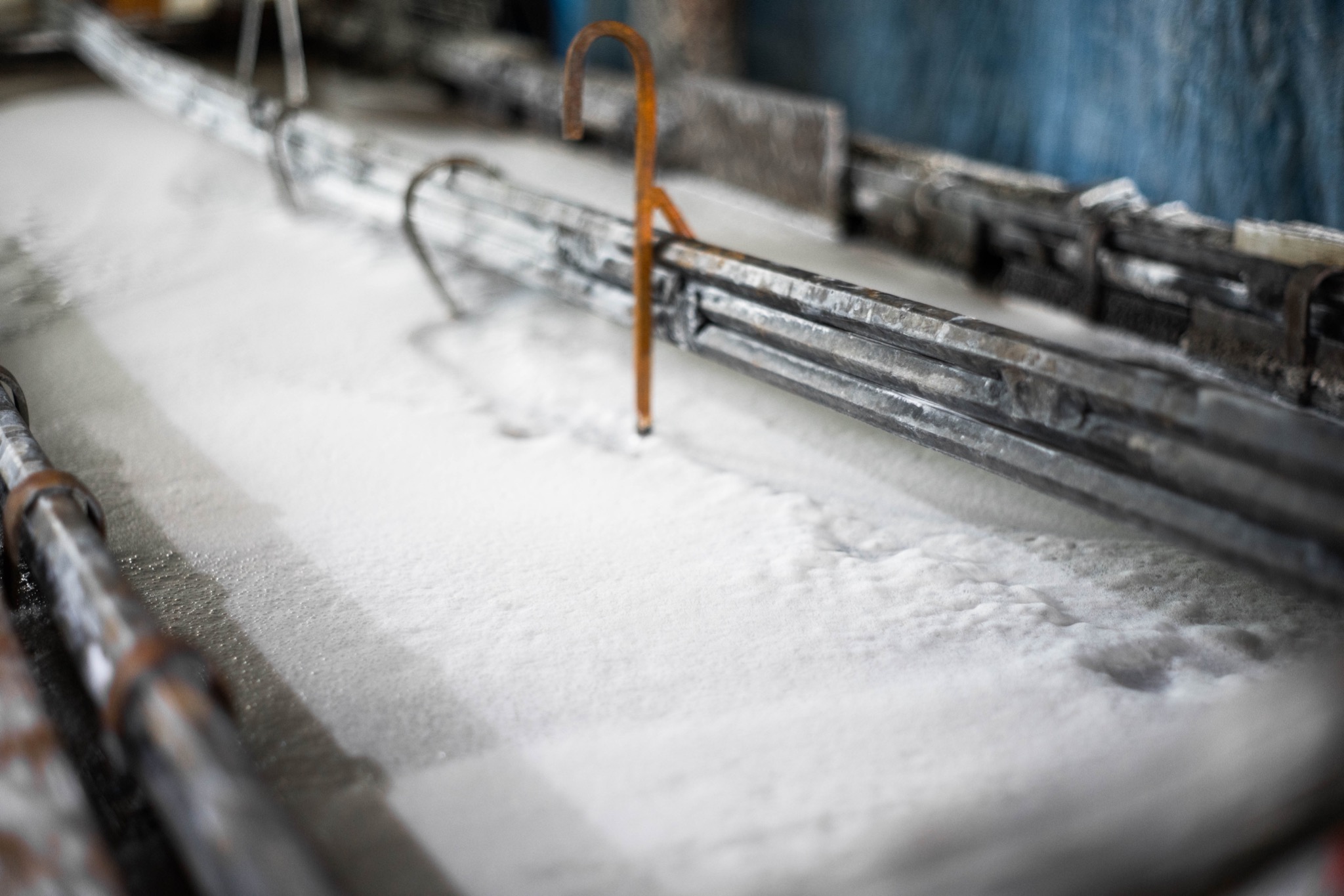 Metalowa konstrukcja zanurzona w białej, pieniącej się cieczy, prawdopodobnie proces czyszczenia lub obróbki powierzchniowej.