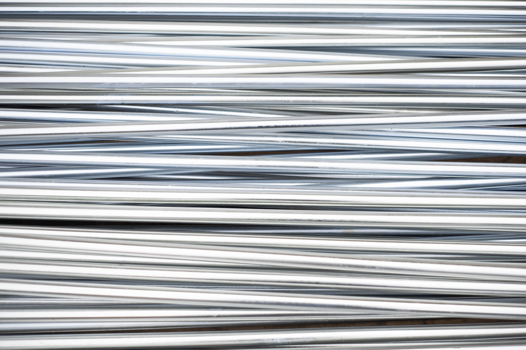 Równolegle ułożone, ocynkowane rury stalowe o gładkiej powierzchni, tworzące wzór powtarzalnych linii z subtelnymi refleksami światła.