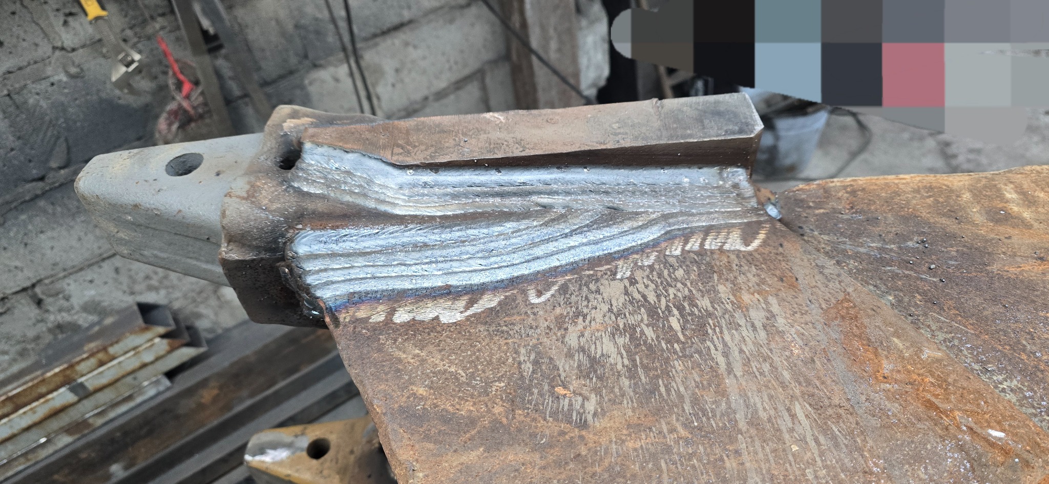 Spoina na metalowym elemencie konstrukcyjnym, widoczne ślady spawania, surowy, warsztatowy charakter. Detal z bliska, oświetlenie naturalne.