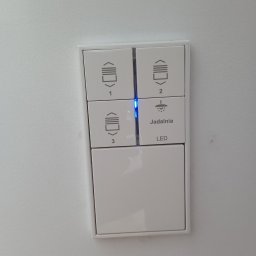 AUTOMATYKA-INSTALACJE ELEKTRYCZNE - PROJEKTY ZENON REMIŚKO - Panel sterowania inteligentnego domu z przyciskami do rolet (1, 2, 3) i oświetlenia (jadalnia), podświetlony diodą LED na białej ścianie.