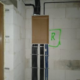 AUTOMATYKA-INSTALACJE ELEKTRYCZNE - PROJEKTY ZENON REMIŚKO - Instalacja elektryczna w trakcie montażu w ścianie z betonu komórkowego. Widoczne kable w peszlach, puszka elektryczna i oznaczenie 'R' na ścianie.