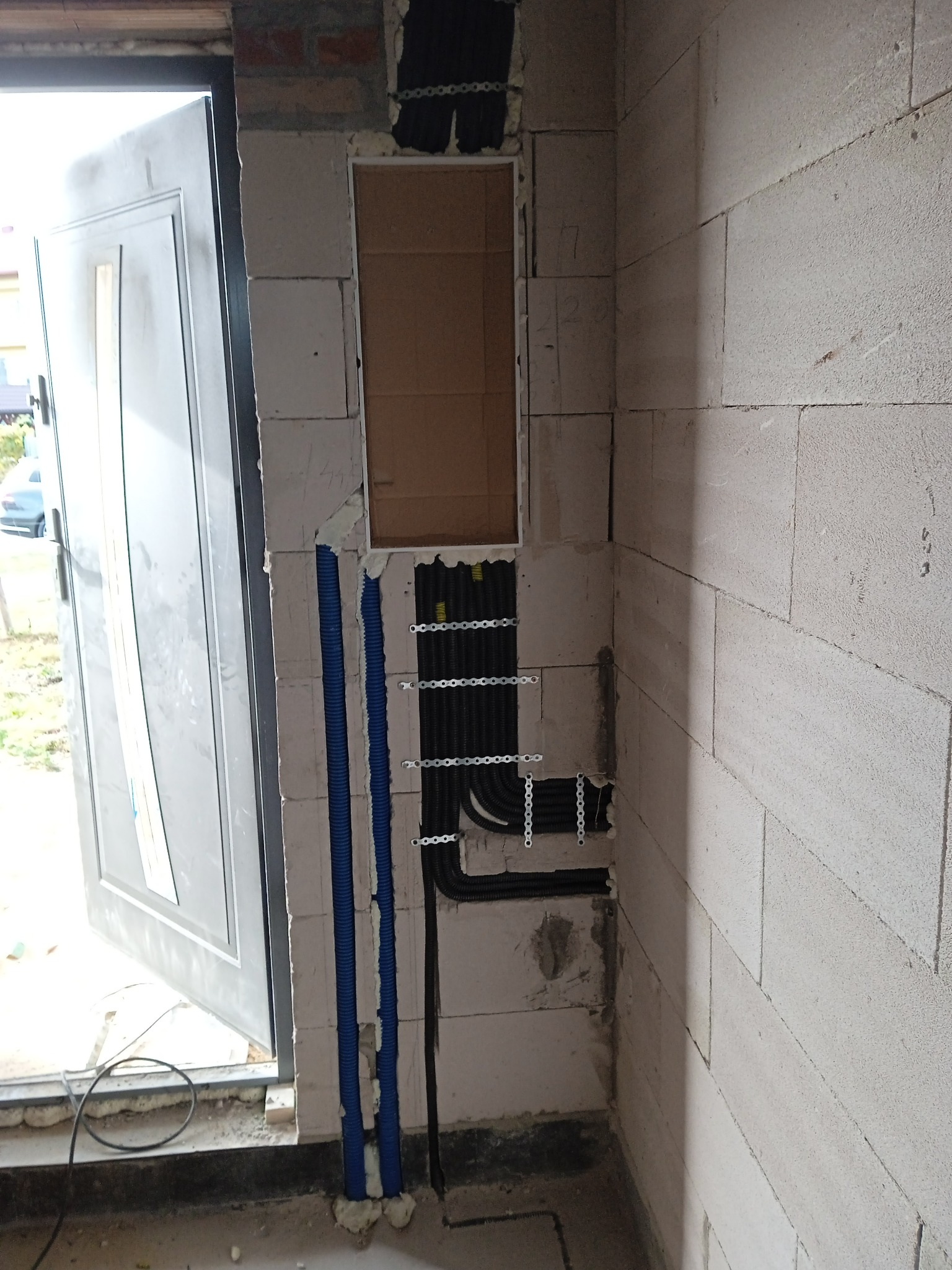 Ściana z instalacją elektryczną w trakcie montażu, widoczne kable w peszlach i puszka podtynkowa. Surowy stan, ściana z betonu komórkowego.