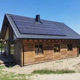 Drewniany dom z ciemną dachówką i panelami słonecznymi na dachu, widok z boku w słoneczny dzień, na trawniku