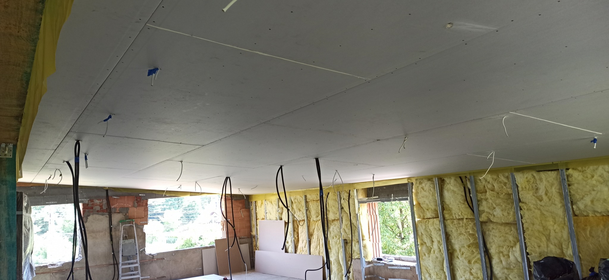 Wnętrze w trakcie prac wykończeniowych: zamontowana płyta karton gips na suficie z widocznymi przewodami elektrycznymi, ocieplone ściany wełną mineralną na metalowym stelażu, częściowo wykończone...