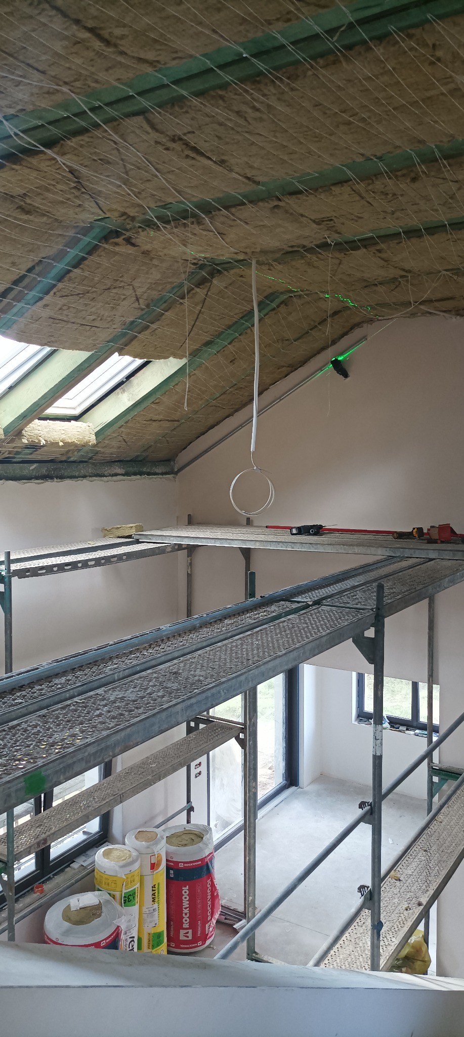 Poddasze w trakcie ocieplania wełną mineralną Rockwool, widoczne rusztowanie, okno dachowe i laserowy niwelator.