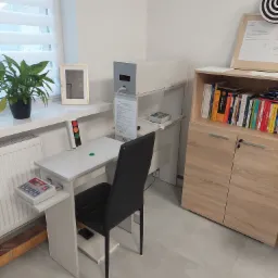 Gabinet lekarski z aparaturą diagnostyczną: stolik z sygnalizacją świetlną, urządzenie pomiarowe, biurko z książkami o tematyce psychologicznej.