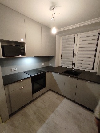 Nowoczesna, szara kuchnia z czarnym blatem i armaturą w Krakowie. Widoczne szafki górne z połyskiem, płyta indukcyjna i piekarnik.