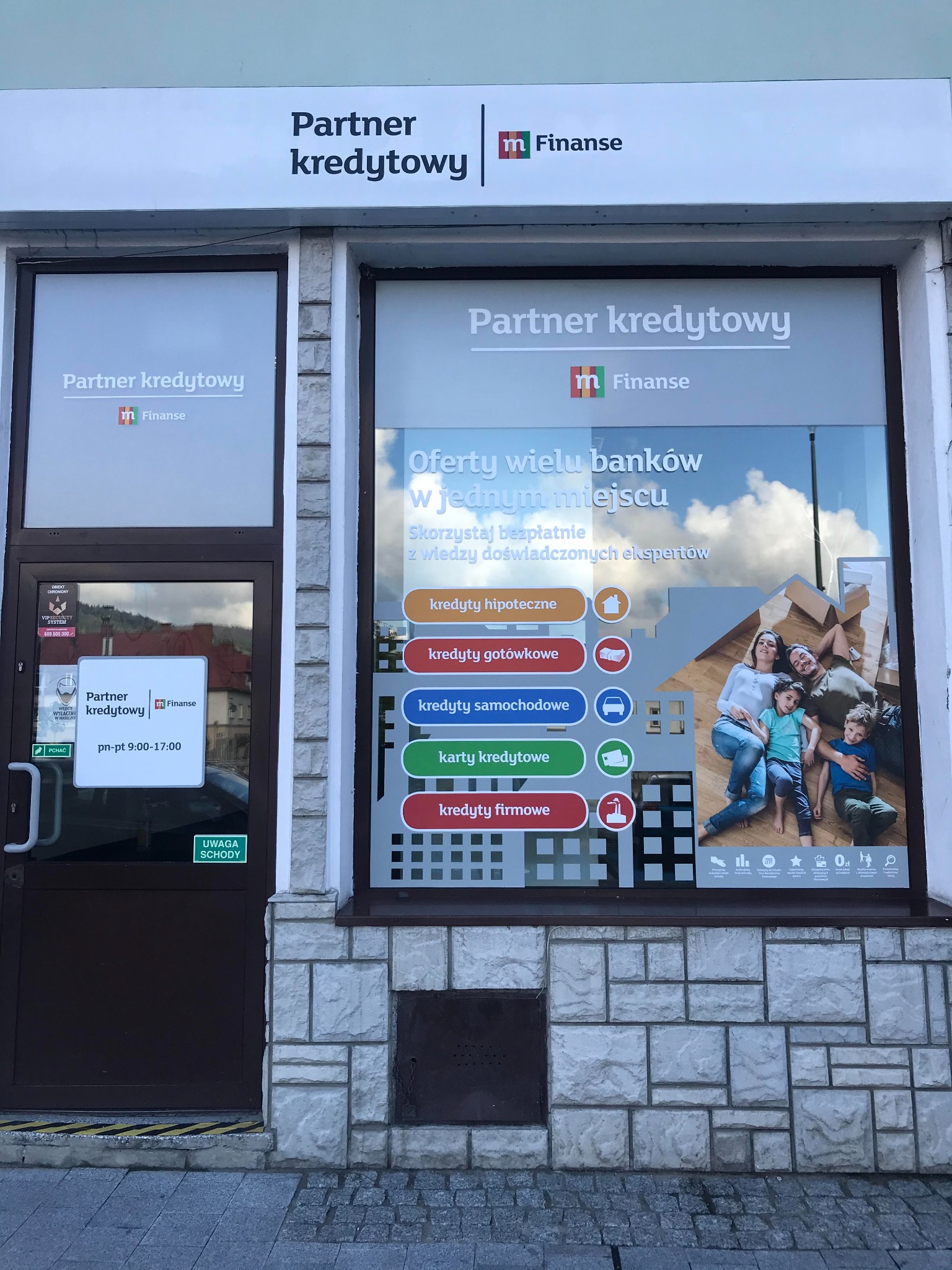 Fasada biura Partner Kredytowy z widocznym logo i plakatem reklamowym prezentującym ofertę kredytową dla rodzin, obejmującą kredyty hipoteczne, gotówkowe, samochodowe i firmowe oraz karty kredytowe.