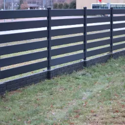 Grafitowe ogrodzenie z poziomych paneli, wsparte na słupkach i podmurówce z cegły, z widokiem na ulicę i autobus w tle.