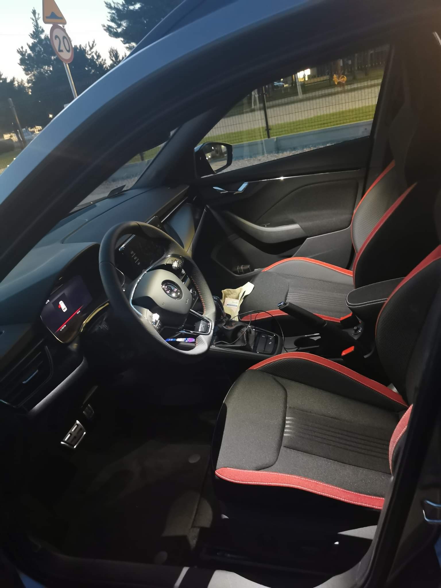 Wnętrze samochodu Skoda z czarnymi fotelami obszytymi czerwoną nicią, widok z zewnątrz na kierownicę i deskę rozdzielczą.