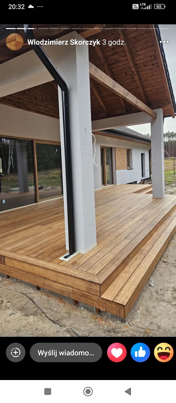 Nowoczesny taras z drewna egzotycznego, zadaszony, z widoczną elewacją domu w jasnych barwach i czarną rynną. Detal wykończenia desek tarasowych.