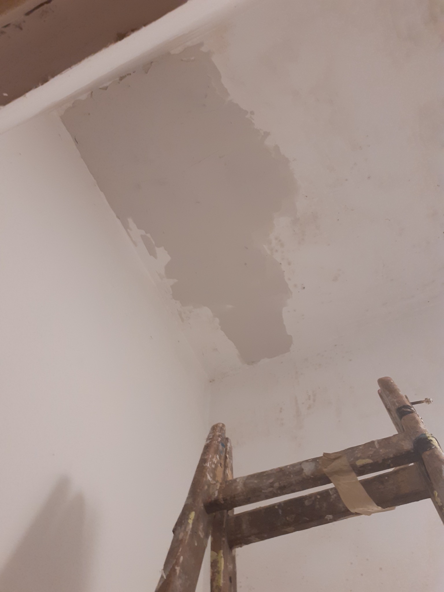 Fragment sufitu po szpachlowaniu, widoczna łata świeżo nałożonej gładzi, drewniana drabina malarska w prawym dolnym rogu kadru.