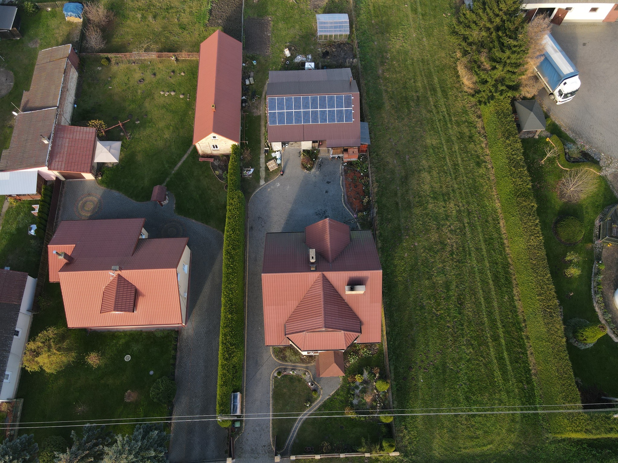 Widok z lotu ptaka na domy jednorodzinne, jeden z nich z panelami słonecznymi na dachu, zaparkowany biały samochód dostawczy w tle.