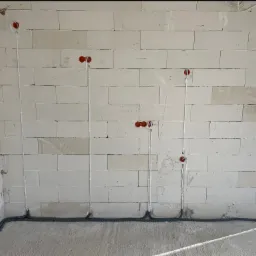 Ściana z betonu komórkowego z widoczną, częściowo zamontowaną instalacją elektryczną w peszlu. Widoczne puszki pod gniazdka i kable.