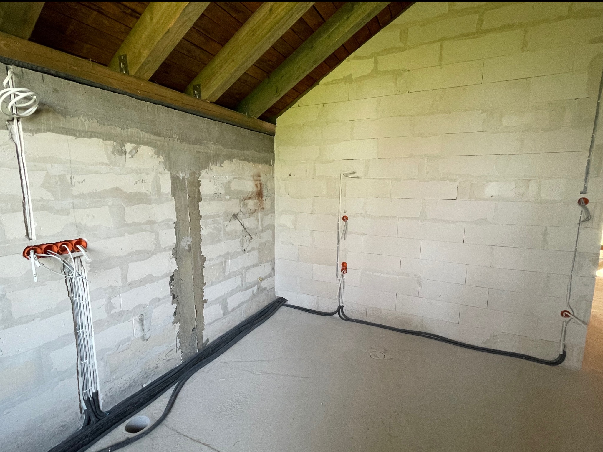 Surowy stan: instalacja elektryczna w nowym budynku z betonowych bloków. Widoczne kable w ścianach i podłodze przed tynkowaniem.