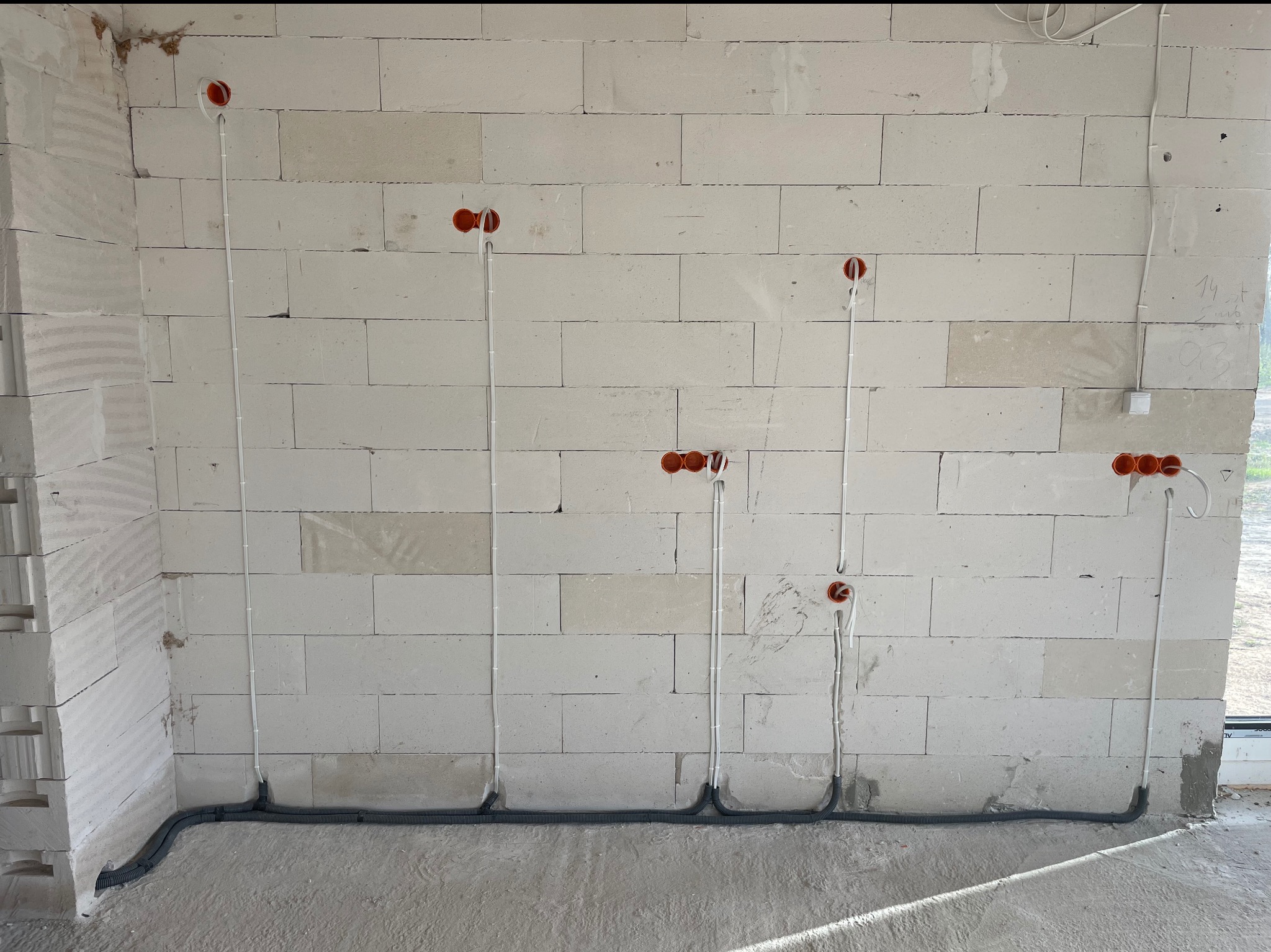 Ściana z betonu komórkowego z widoczną, częściowo zamontowaną instalacją elektryczną w peszlu. Widoczne puszki pod gniazdka i kable.