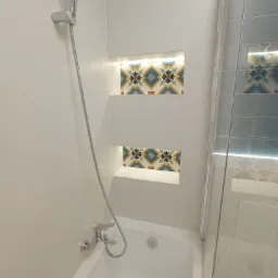 Biała łazienka z wanną, szklanym parawanem i wnękami z dekoracyjnymi płytkami podświetlonymi ledami, armatura chromowana.