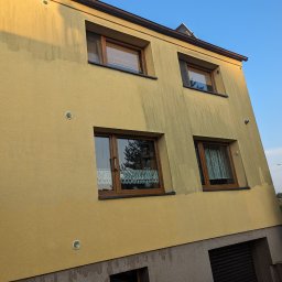 Ewa Klimek Klim-Majster - Żółta elewacja dwupiętrowego domu z brązowymi oknami, widoczne ślady po czyszczeniu, tworzące kontrast z nieoczyszczonymi fragmentami, ukazujące efekt przed i po.