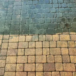 Częściowo wyczyszczona kostka brukowa, widoczny kontrast między brudną, ciemną powierzchnią a czystą, jasnobrązową częścią.