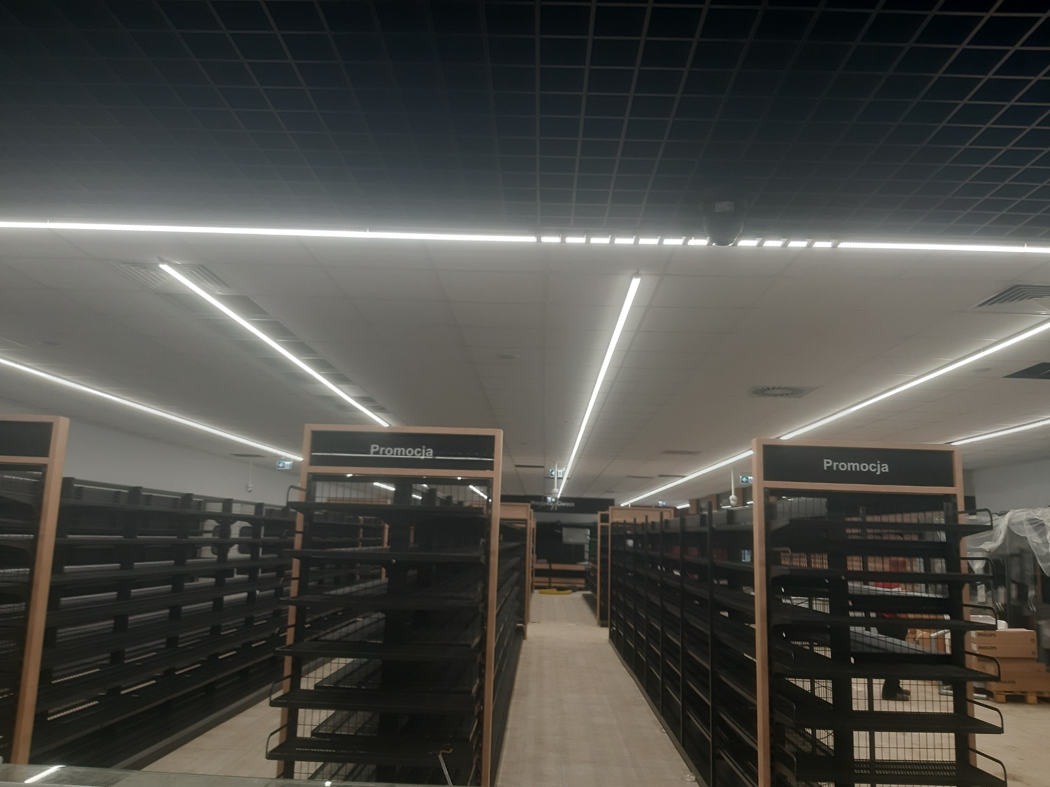 Rzędy pustych, metalowych regałów sklepowych z napisem 'Promocja' pod oświetleniem LED w nowym obiekcie handlowym.