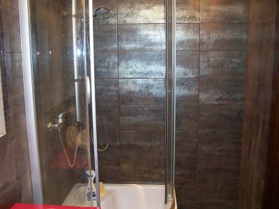 Kabina prysznicowa z przesuwnymi drzwiami, wykończona ciemnymi, metalizowanymi płytkami w kwadratowym formacie, widoczna bateria i słuchawka prysznicowa.