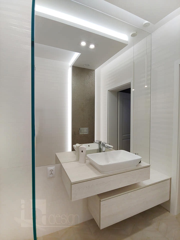 Nowoczesna łazienka z wiszącą szafką pod umywalkę z jasnego drewna, prostokątną umywalką nablatową i dużym lustrem z podświetleniem LED, widok na ścianę z mozaiką w tle.